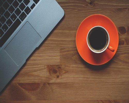 A laptop and a cup of coffee on a wooden desk